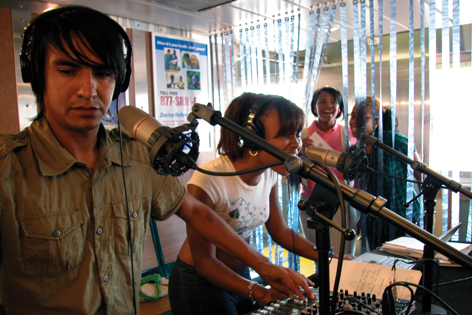 The FM Ferry Experiment studio on the John J. Marchi Staten Island Ferry. Image features (left to right) Angel Nevarez of neuroTransmitter, and ferry rider Sheria Washington singing on-air; friends/ferry riders listening in.